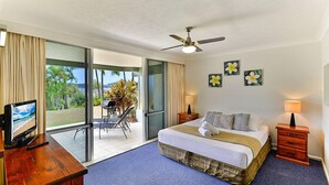 A hotel room with a bed, a desk with a TV, a ceiling fan, and a view of the outdoors. - Hibiscus 006 (Whitsundays)