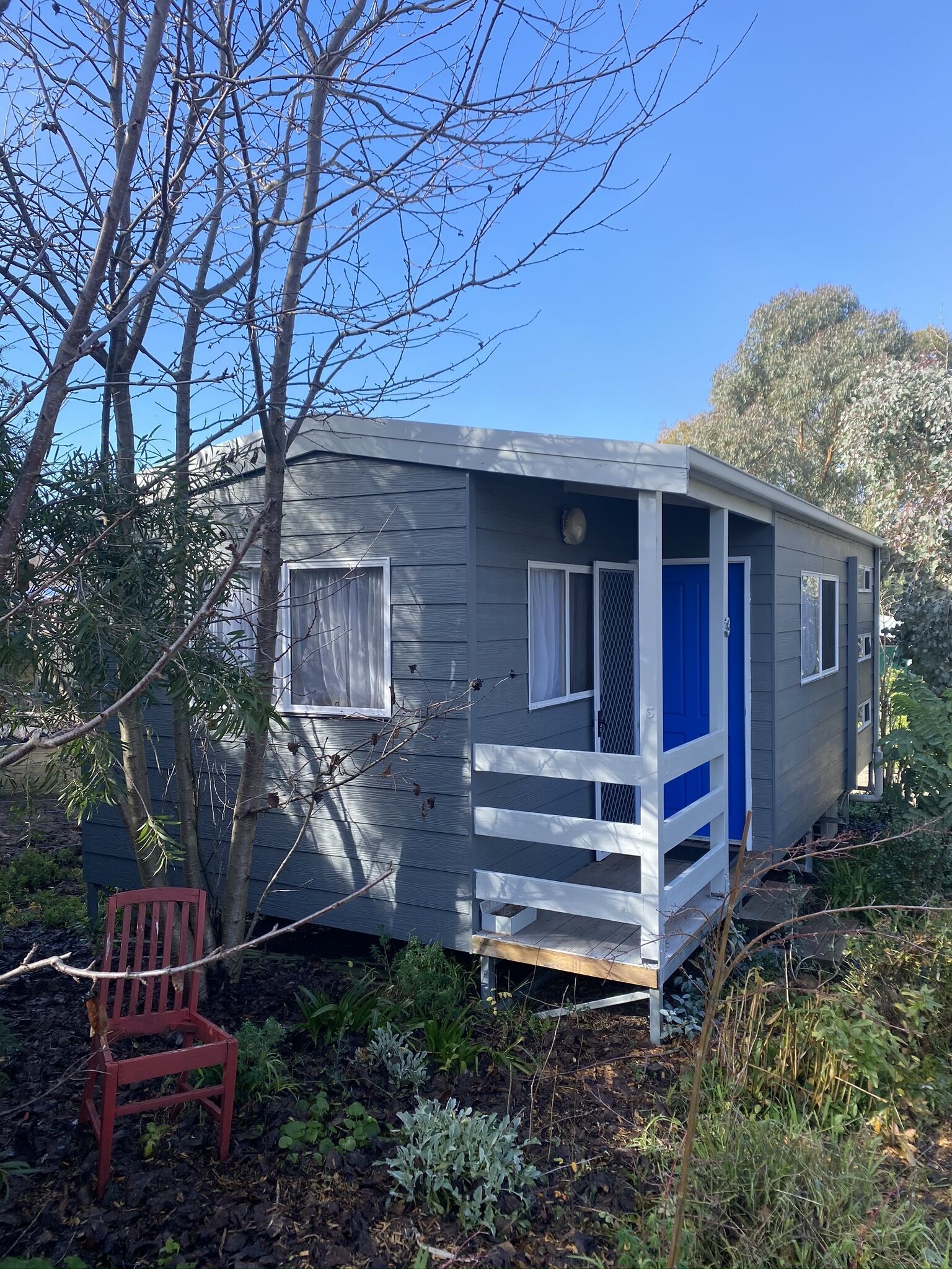 A small, single-story cabin with a porch, surrounded by trees and vegetation.