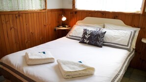 Una cama bien hecha con dos toallas dobladas, una lámpara de noche y un cojín estampado con motivos florales.