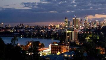 A cityscape at dusk with illuminated buildings, a river in the foreground, and a mix of residential and commercial structures.