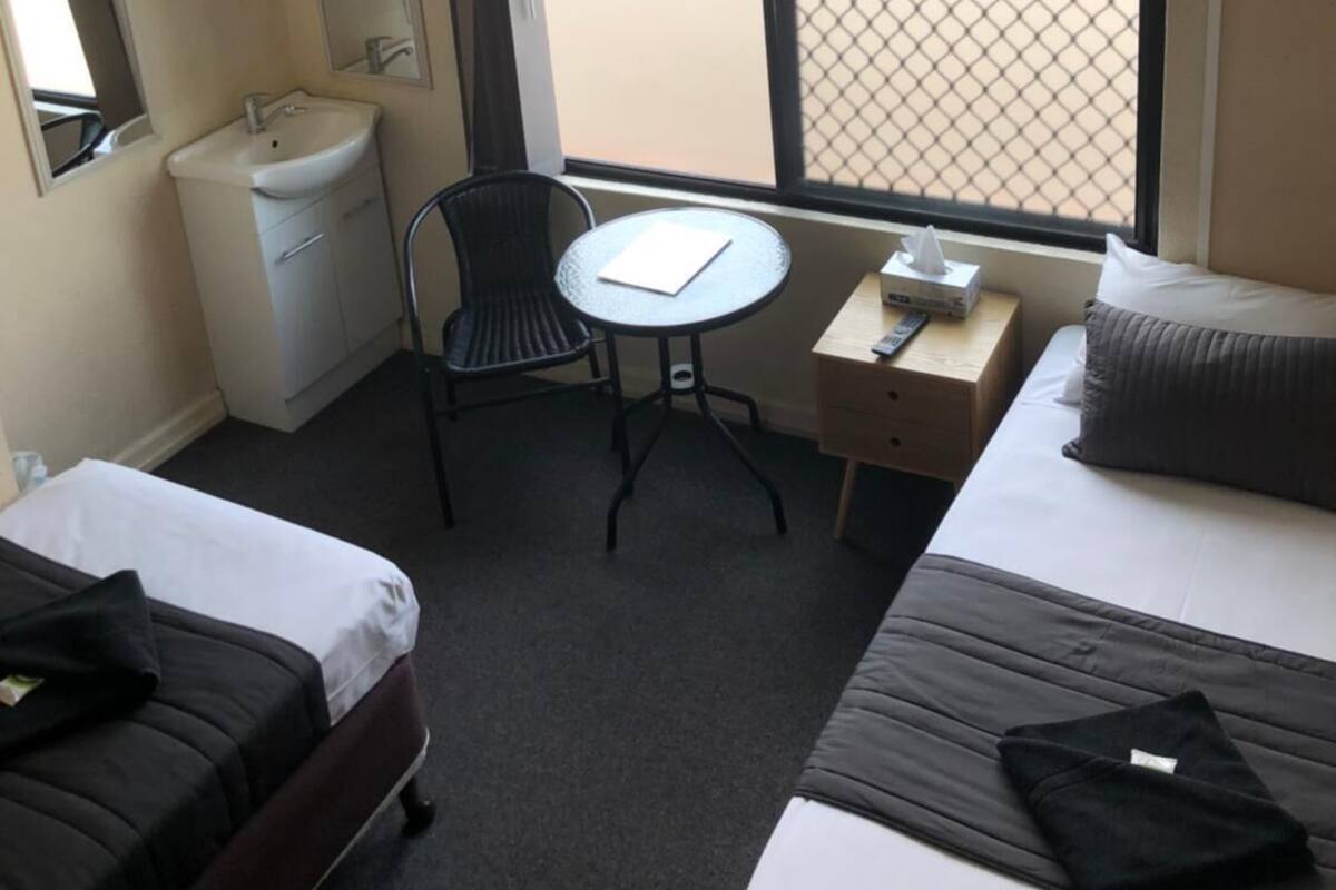 A hotel room with a bed, a desk with a chair, a small table, a sink, and a window with a view.