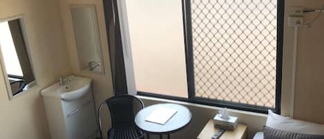 A hotel room with a bed, a desk with a chair, a small table, a sink, and a window with a view.