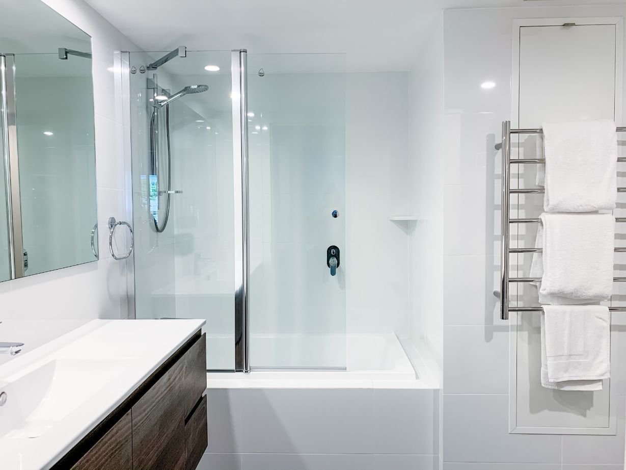 A modern bathroom with a glass-enclosed shower, a white bathtub, and a vanity with a mirror.
