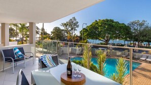 A balcony with a pool view, outdoor seating, and a bottle of wine on a table.