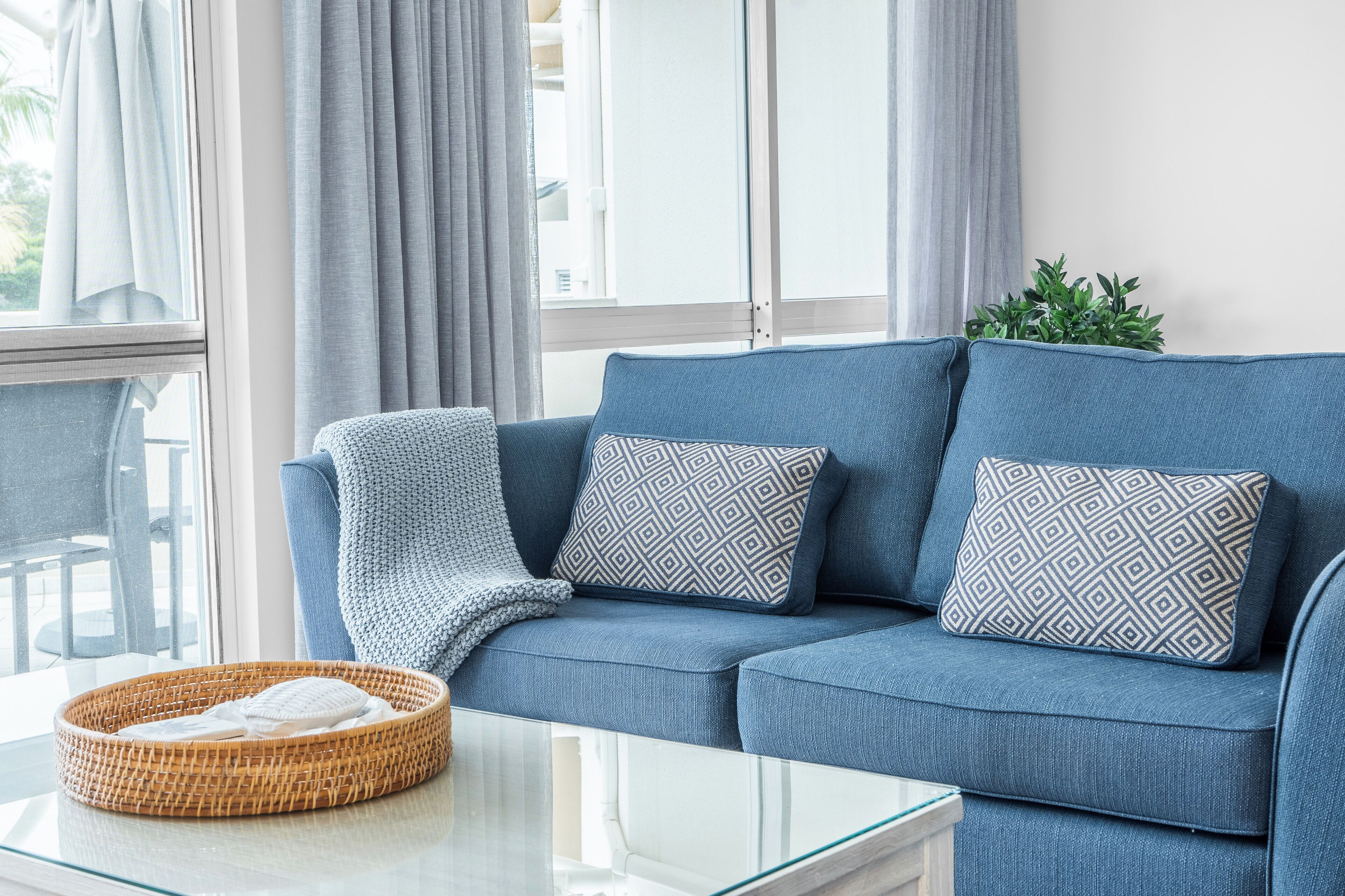 A blue sofa with patterned cushions, a wicker basket with a white towel, and a potted plant.
