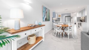 A modern kitchen with white cabinetry, a wooden countertop, and a dining area with white chairs.