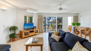 A modern living room with a sofa, a coffee table, a TV, and a dining area with chairs and a table.