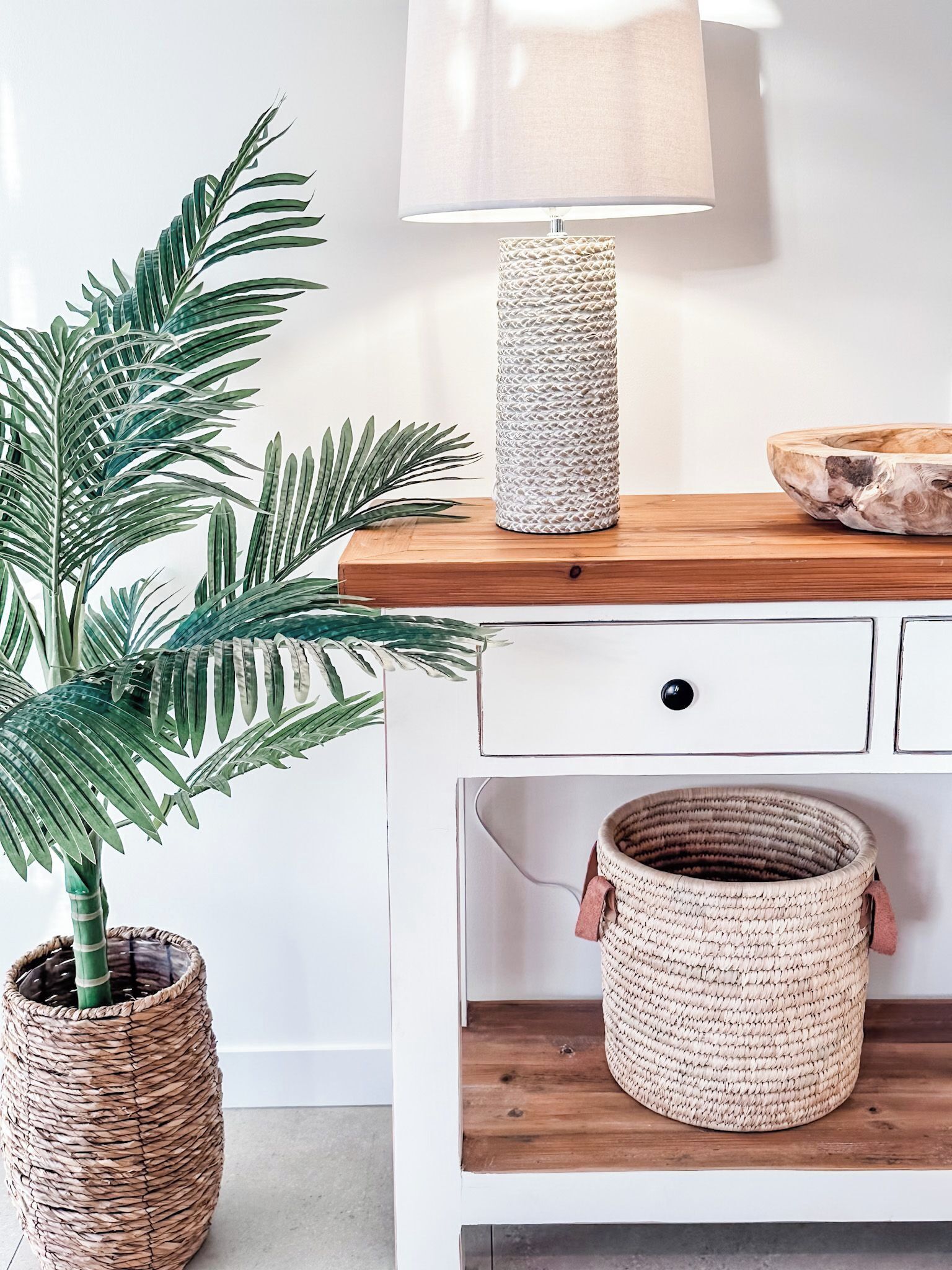 Une pièce comprenant un buffet en bois, une lampe, une plante en pot et des paniers tressés.