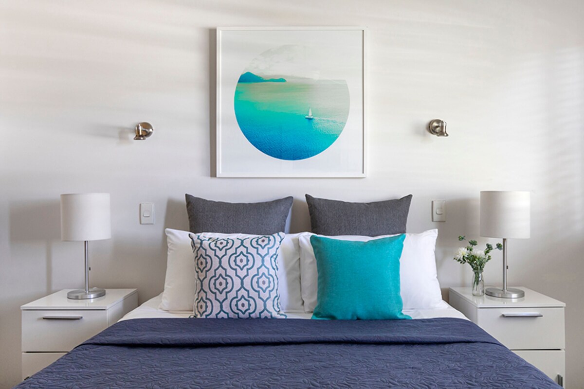 A neatly arranged bedroom with a bed, two bedside tables, and a wall-mounted picture.