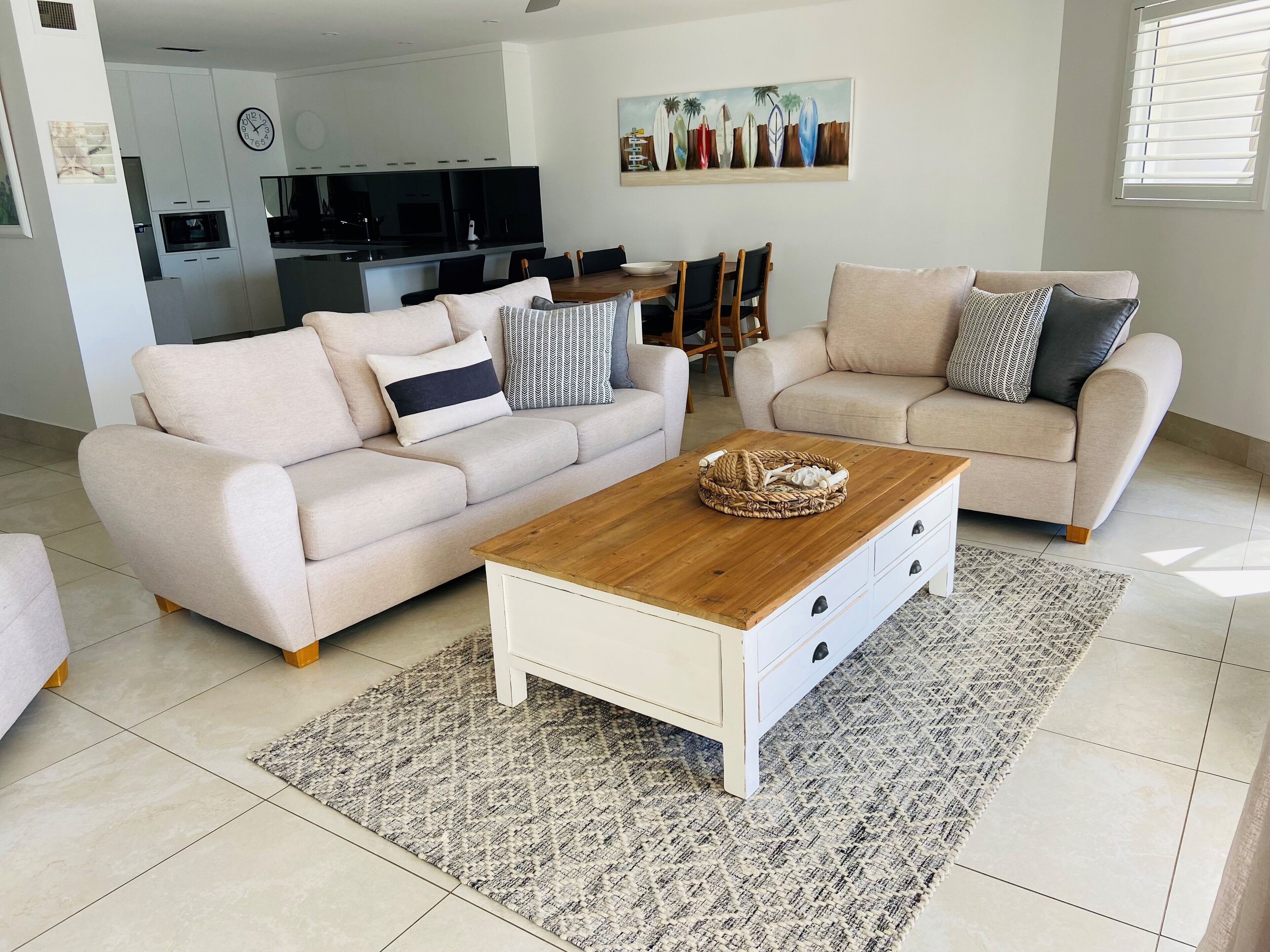 Ein modernes Wohnzimmer mit zwei beigen Sofas, einem Holztisch und einer Küche im Hintergrund.