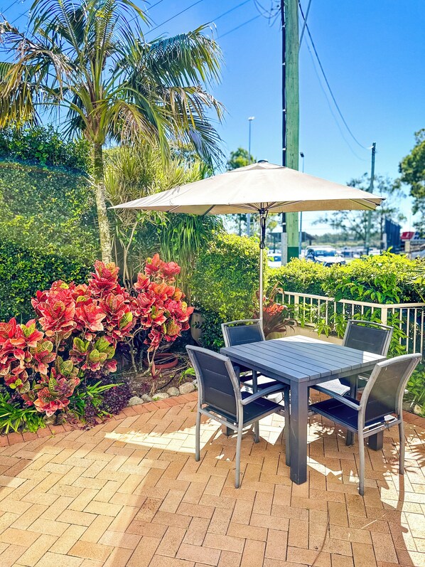 Un patio al aire libre con una mesa y sillas, rodeado de exuberante vegetación y una palmera.