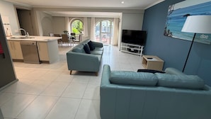 A modern living room with a sofa, a TV, and a dining area with chairs and a table. - Korora Bay Village Resort (Korora)