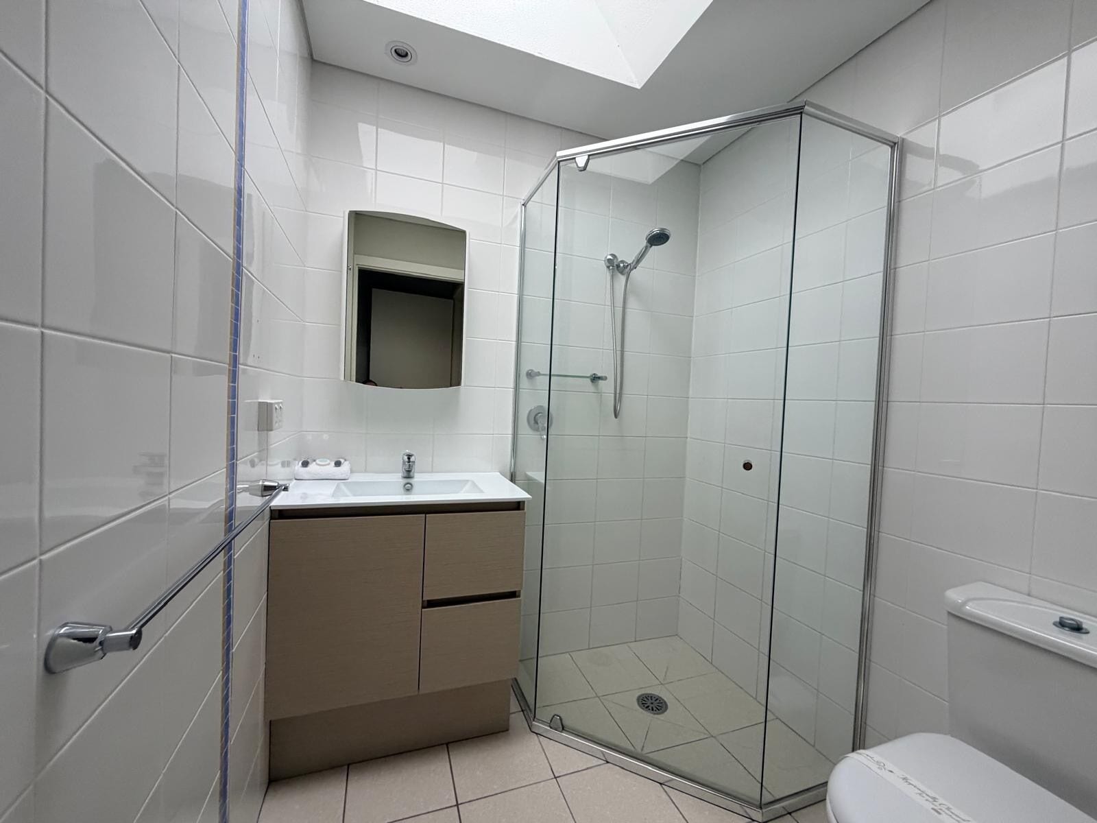 Un baño moderno con ducha separada por vidrio, tocador con lavamanos y retrete.