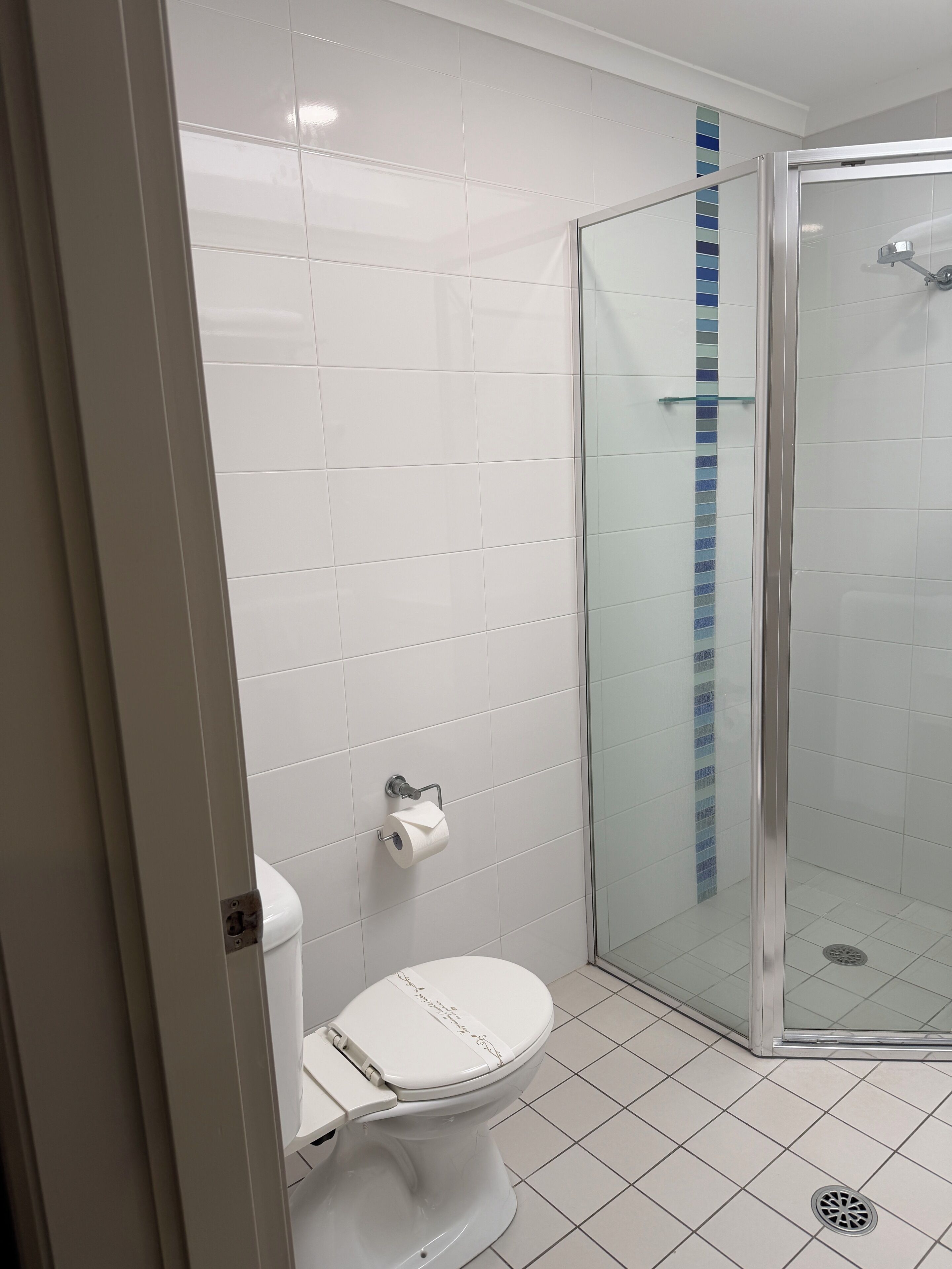 A bathroom with a toilet, a glass shower enclosure, and a tiled floor.