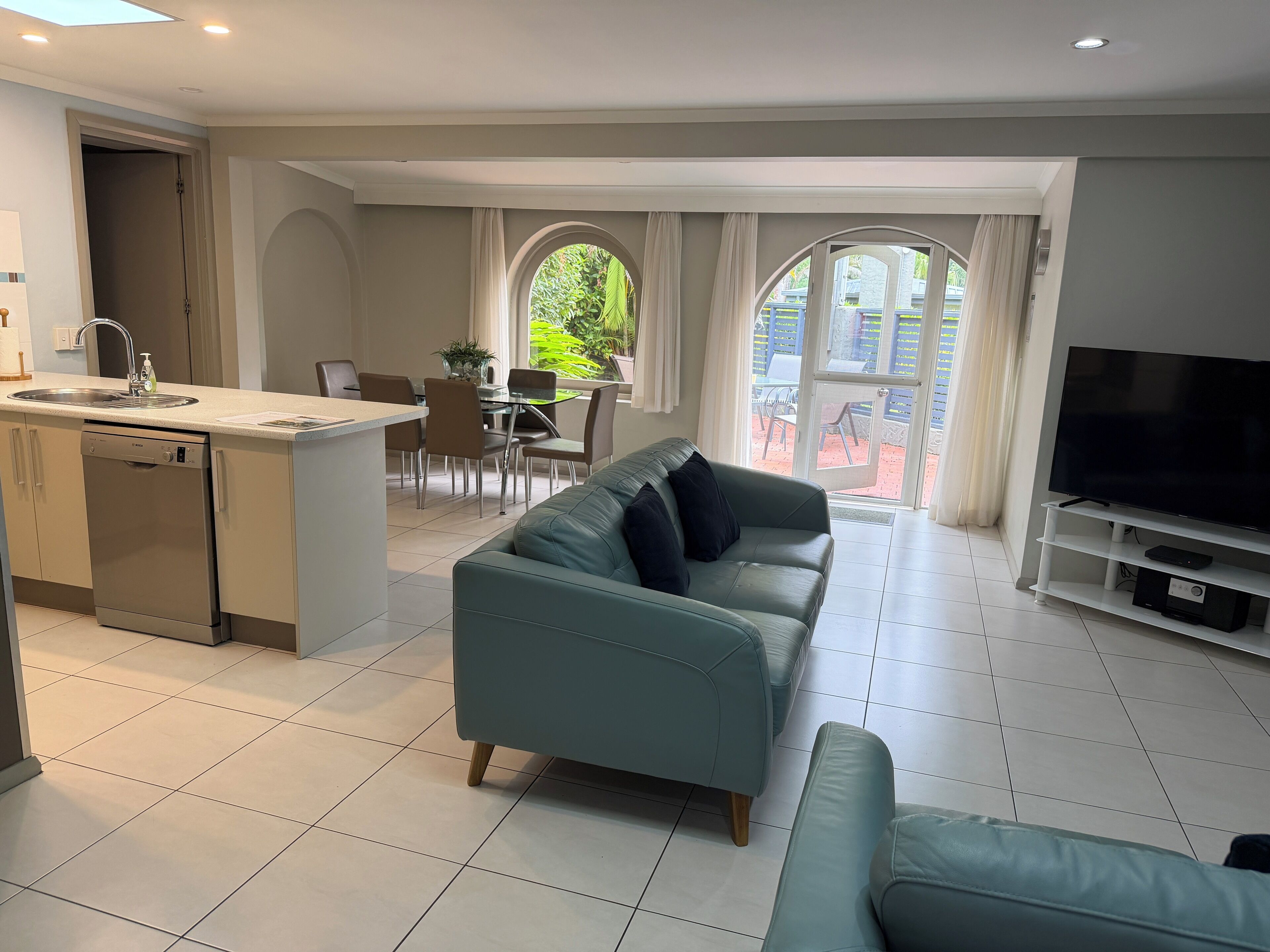 A modern living room with a sofa, TV stand, and a dining area with chairs and a table.