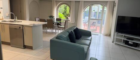 A modern living room with a sofa, TV stand, and a dining area with chairs and a table.