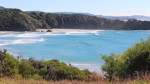 A coastal landscape with a beach, clear blue waters, and dense greenery. - Korora Bay Village Resort (Korora)