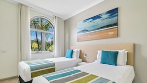 A hotel room with two beds, a large window with curtains, a beach-themed painting, and a view of palm trees. - Korora Bay Village Resort (Korora)
