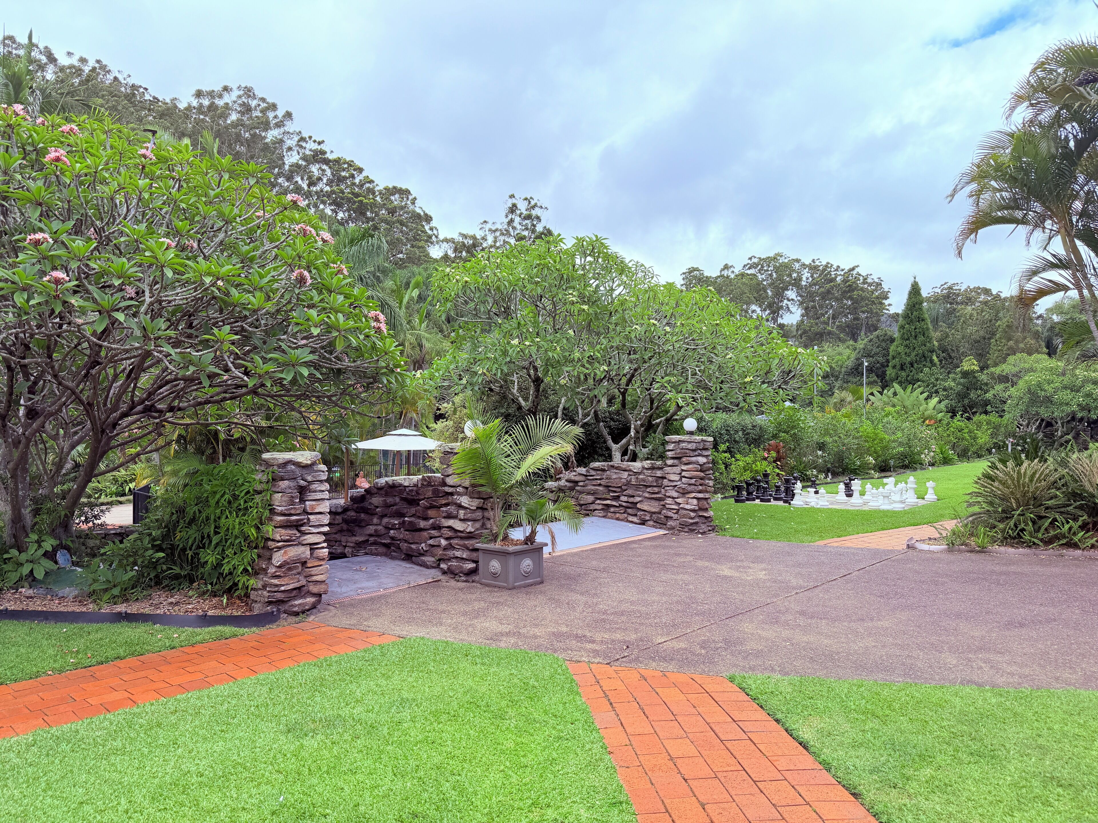 A landscaped garden with a stone archway, a paved walkway, and various greenery.