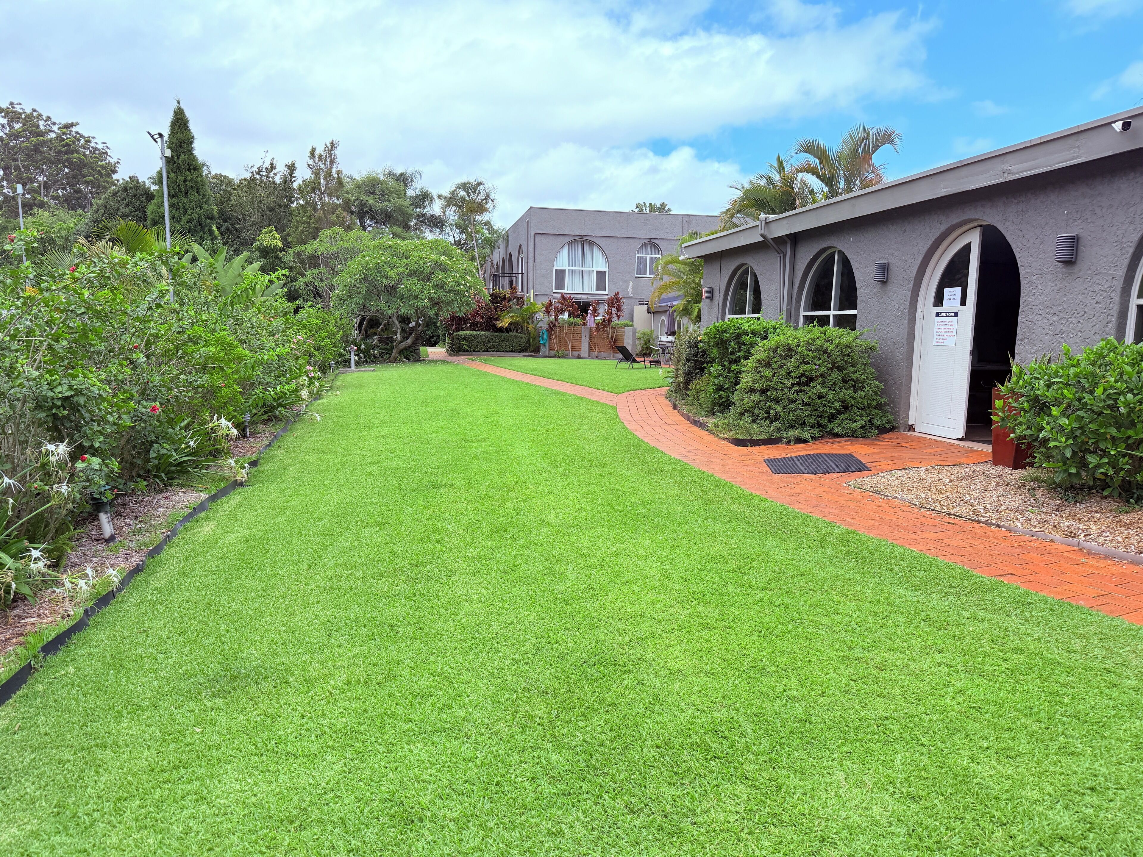 A well-maintained garden with a pathway leading to a building with arched windows and a sign indicating a "CAMERA ROOM".