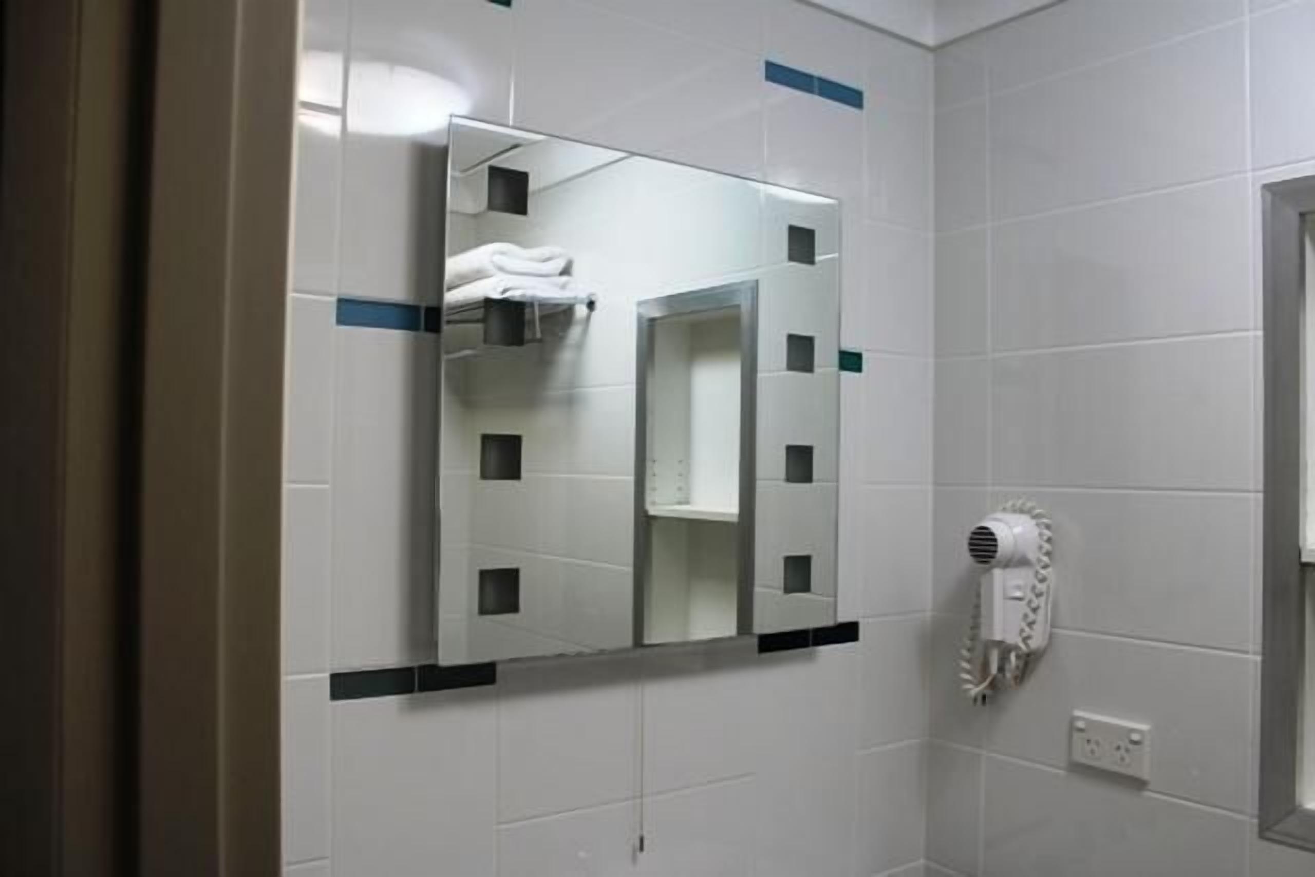 A bathroom with white tiled walls, a mirror, a towel rack, and a hairdryer.