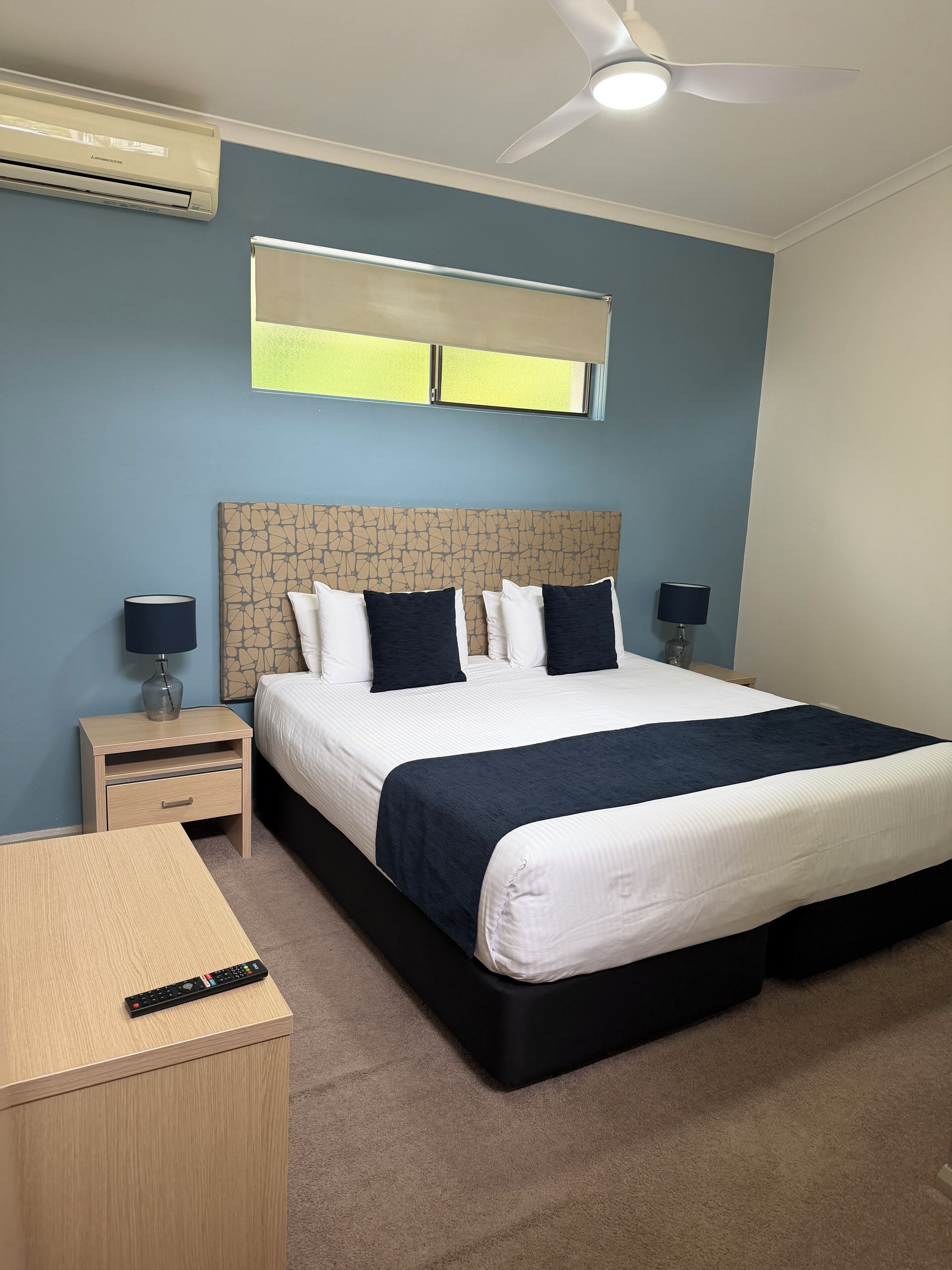 A bedroom with a bed, two bedside tables, a ceiling fan, and an air conditioning unit.