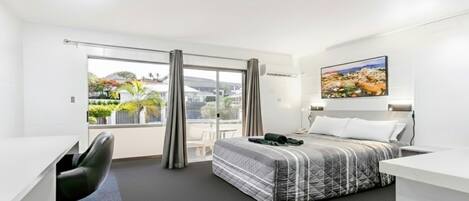 A modern hotel room with a bed, a desk, a chair, and a large window offering a view of the outdoors.