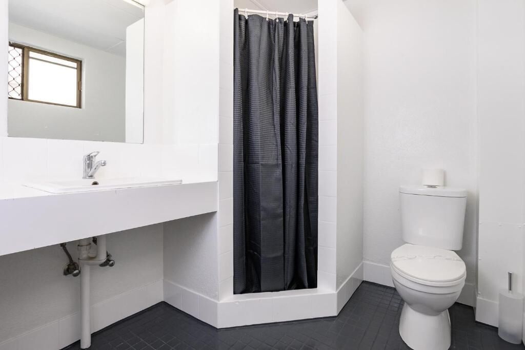 Une salle de bain avec un lavabo blanc, un miroir, un rideau de douche noir et des toilettes blanches.
