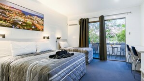 Habitación de hotel con dos camas, un balcón con mesa y sillas, y un ventanal con cortinas.