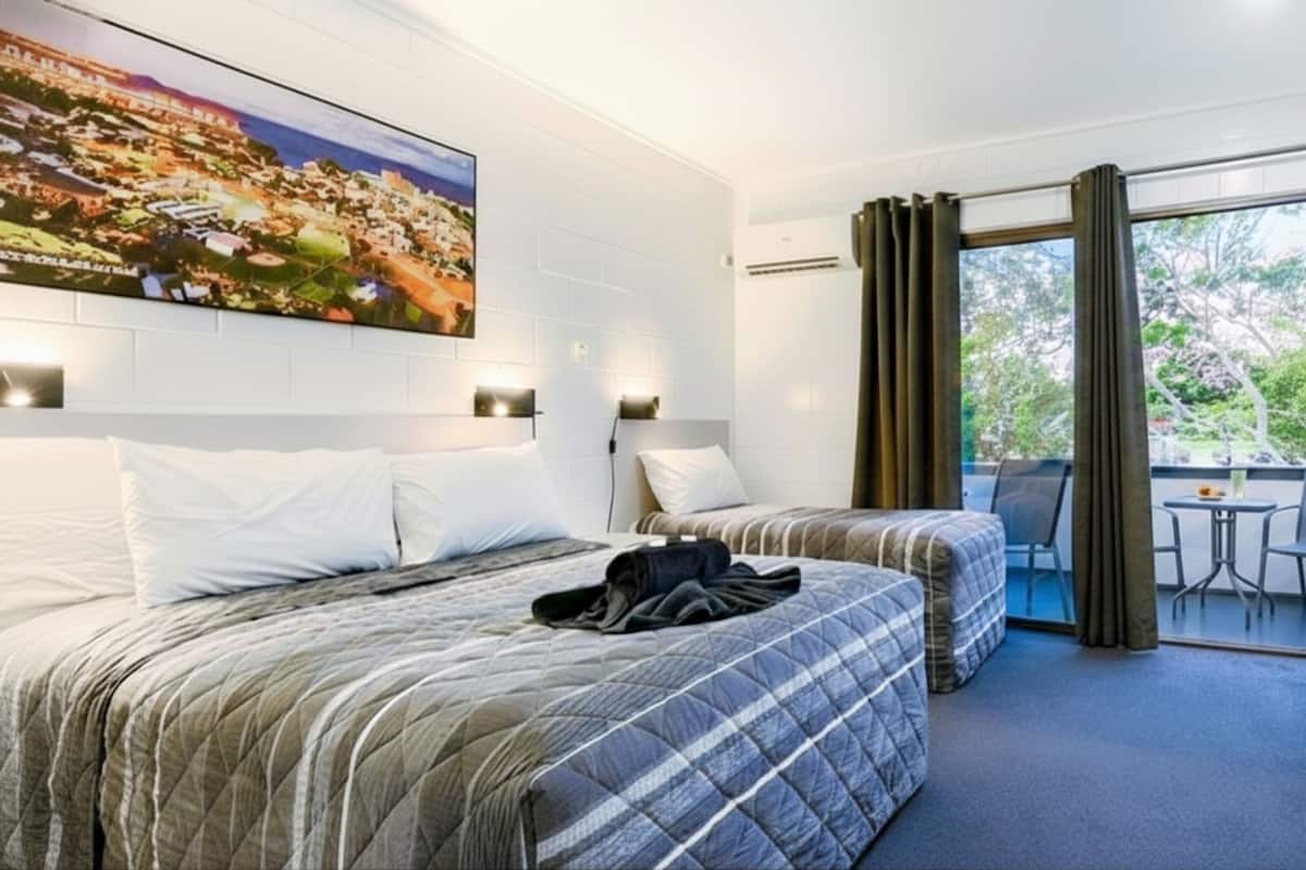 A hotel room with two beds, a balcony with a table and chairs, and a large window with curtains.