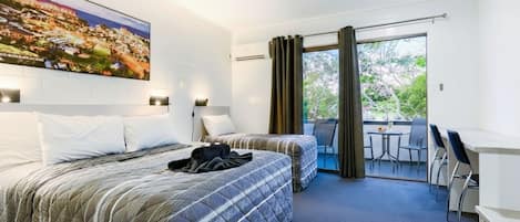 A hotel room with two beds, a balcony with a table and chairs, and a large window with curtains.