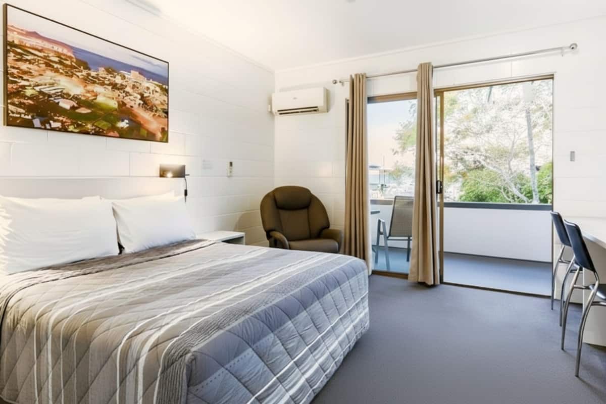 A hotel room with a bed, a desk, a chair, and a balcony with a view.