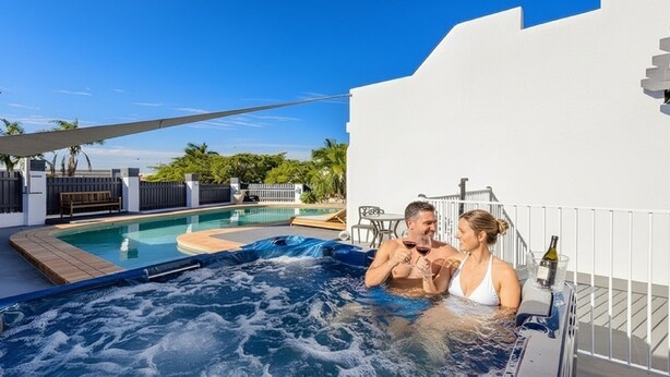 Una pareja relajándose en un jacuzzi con piscina y zona de estar al aire libre.