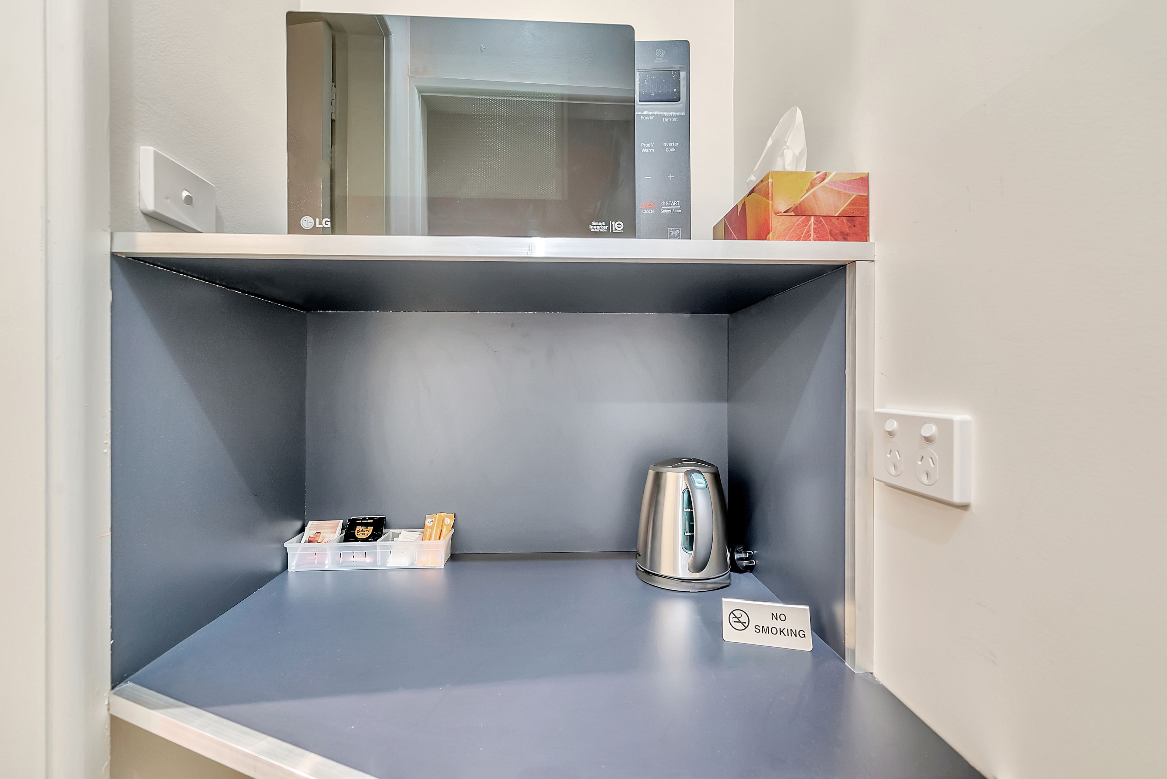 Une petite cuisine équipée d’un four à micro-ondes, d’une bouilloire et d’un panneau indiquant qu’il est interdit de fumer.