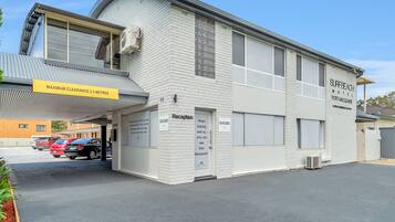 Un edificio blanco con un letrero que dice "SURFBEACH MOTEL PORT MACQUARIE" y un letrero que indica "RECEPción". Hay un cartel amarillo que muestra "ALTURA MÁXIMA 2.3 METROS".