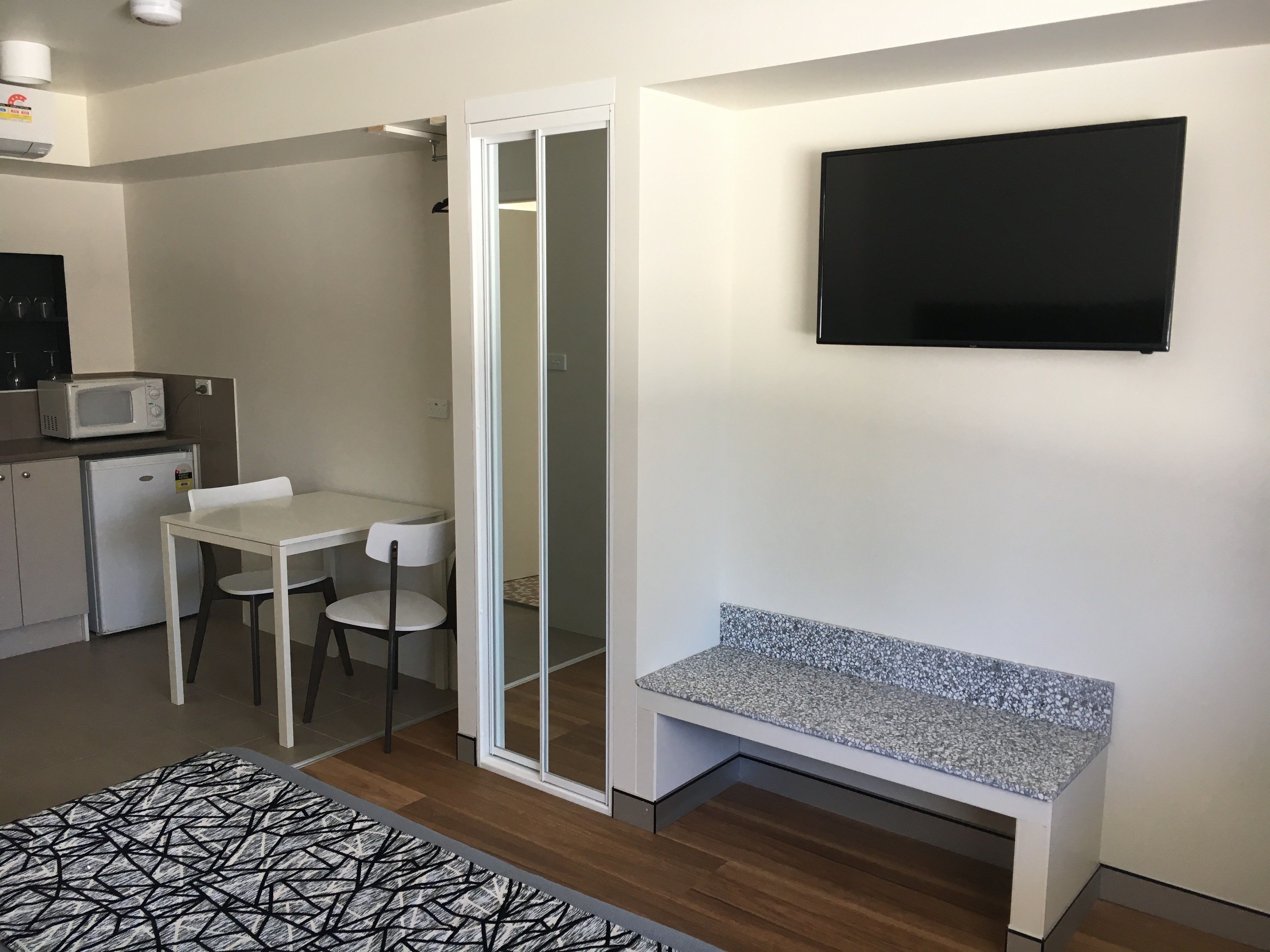A compact living space with a kitchenette, a dining area, a shower, and a seating bench.