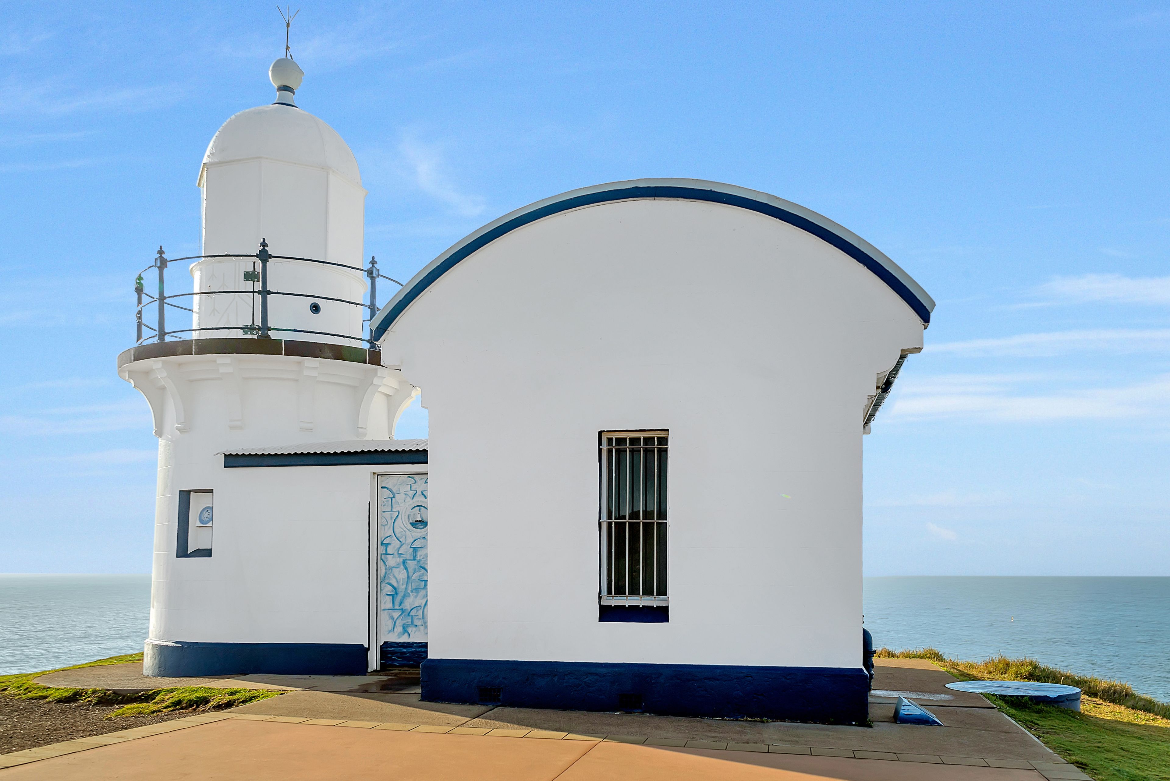 A white lighthouse with a blue trim and a dome, situated by the sea.