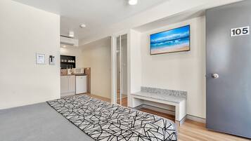 A modern hotel room with a bed, a bench, a TV, and a door marked 105.