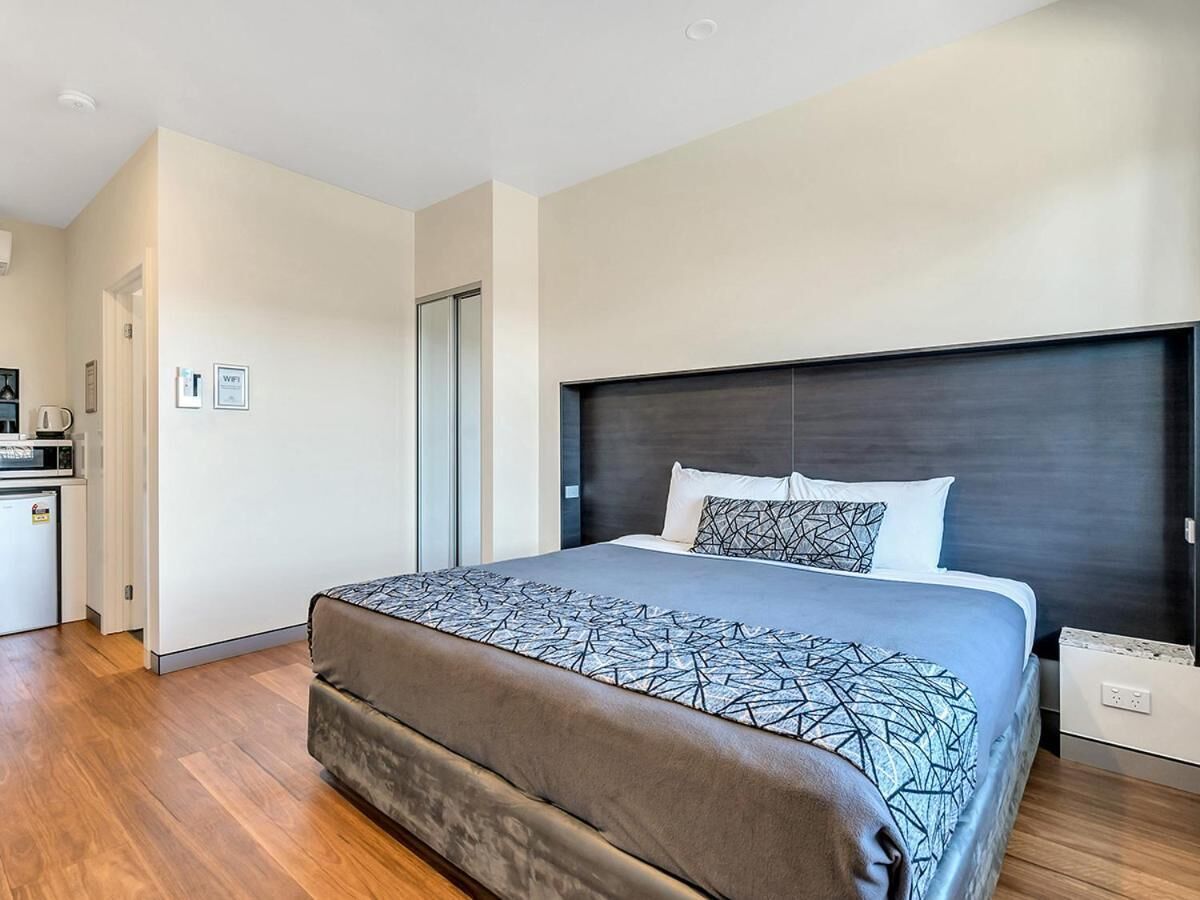 Un dormitorio moderno con una cama grande, un cabecero oscuro y suelo de madera.