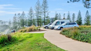 A pathway leading to a parking area with a blue car, surrounded by greenery and tall trees. - Surf Beach Motel Port (Port Macquarie)