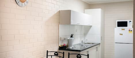 A compact kitchen with a wooden table and chairs, white cabinets, a microwave, and a clock on the wall.