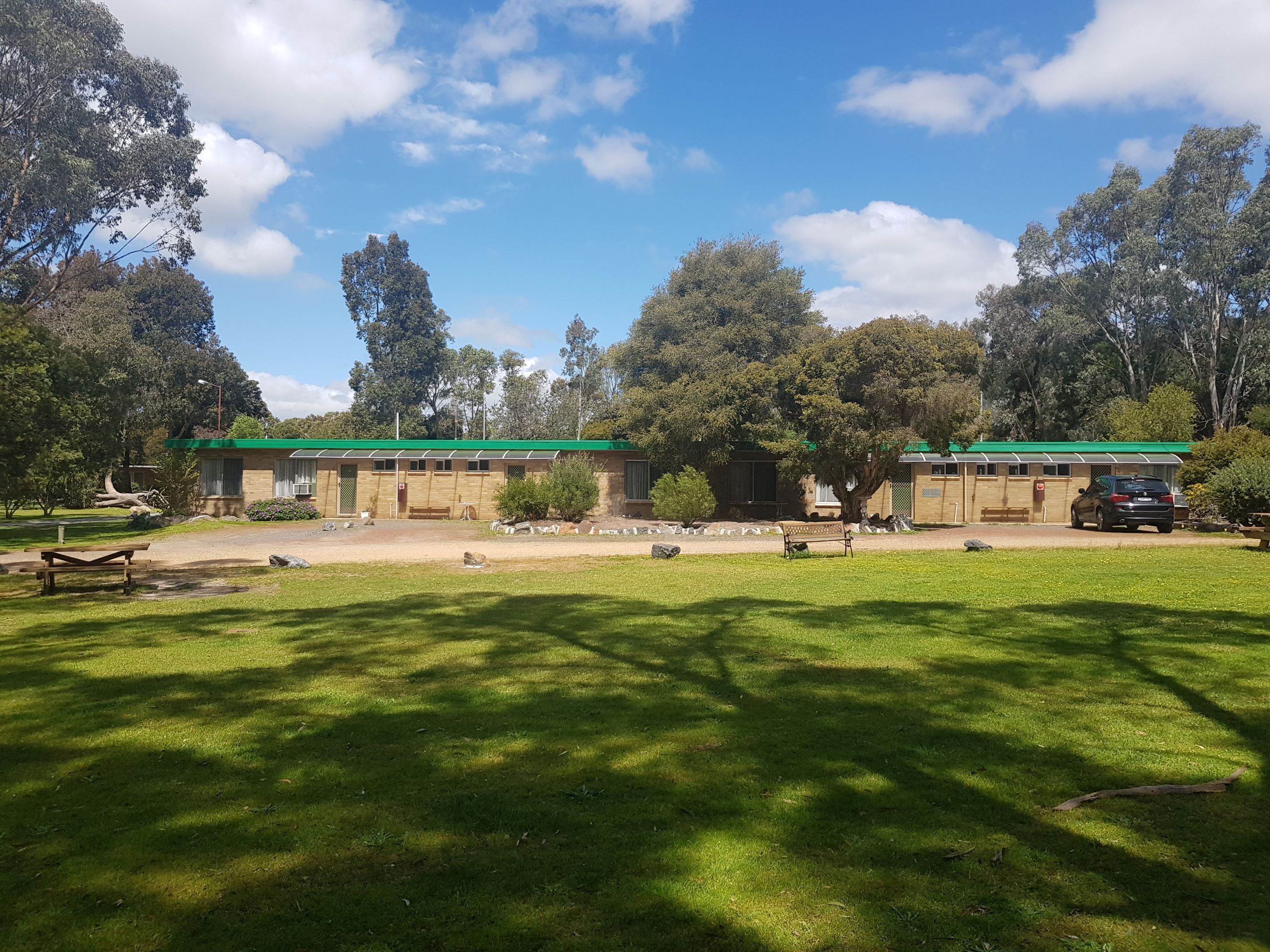 A building with a green roof, surrounded by trees and a grassy area with benches.