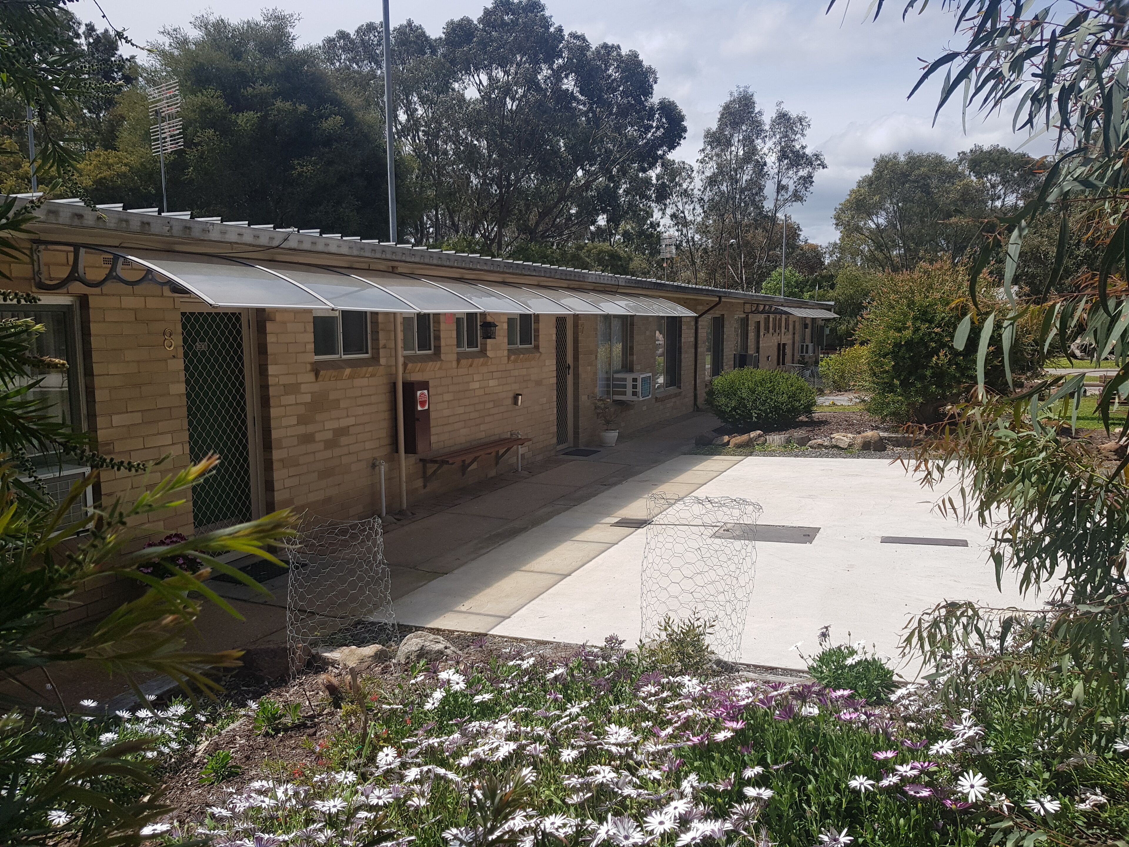 A building with a brick facade, a covered walkway, and a garden with flowers.