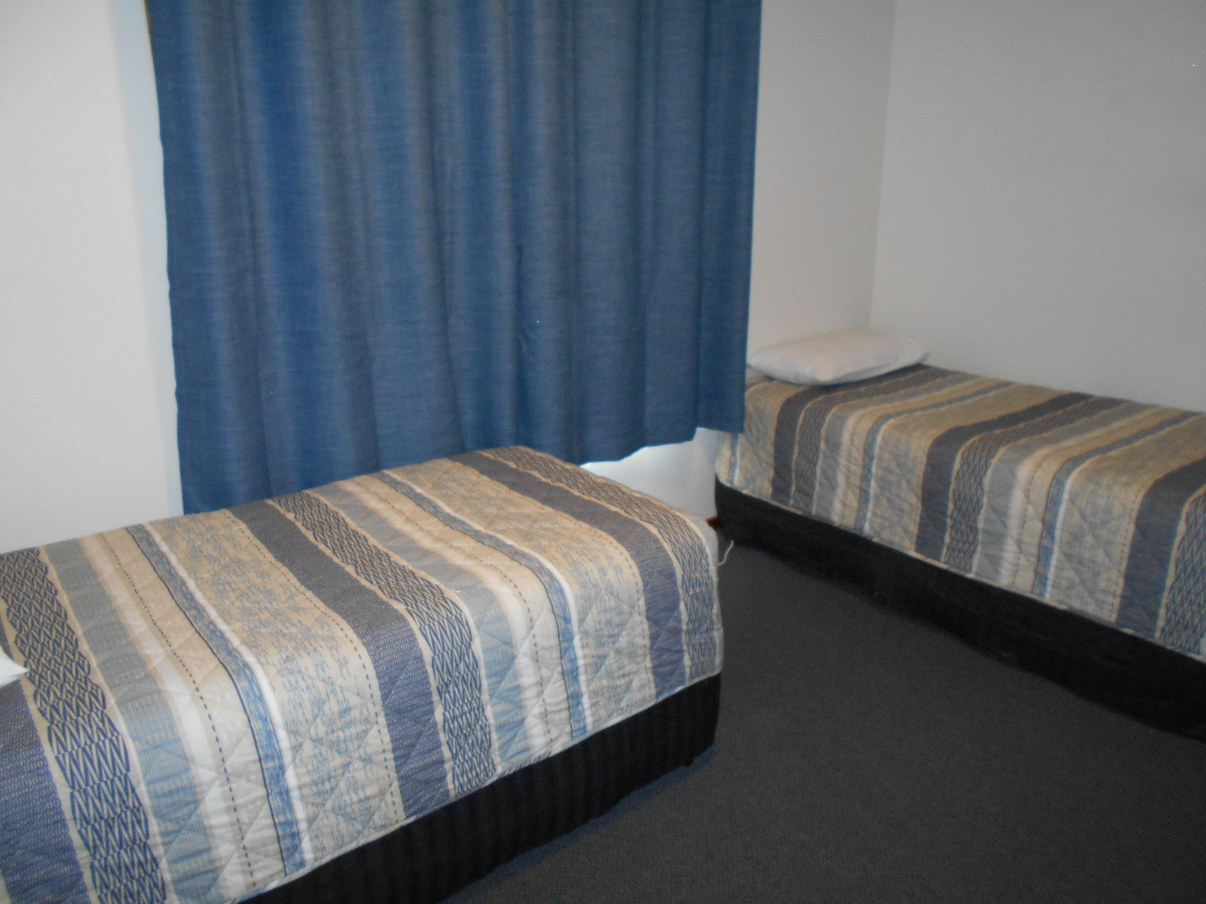 A room with two single beds, a blue curtain, and a plain white wall.