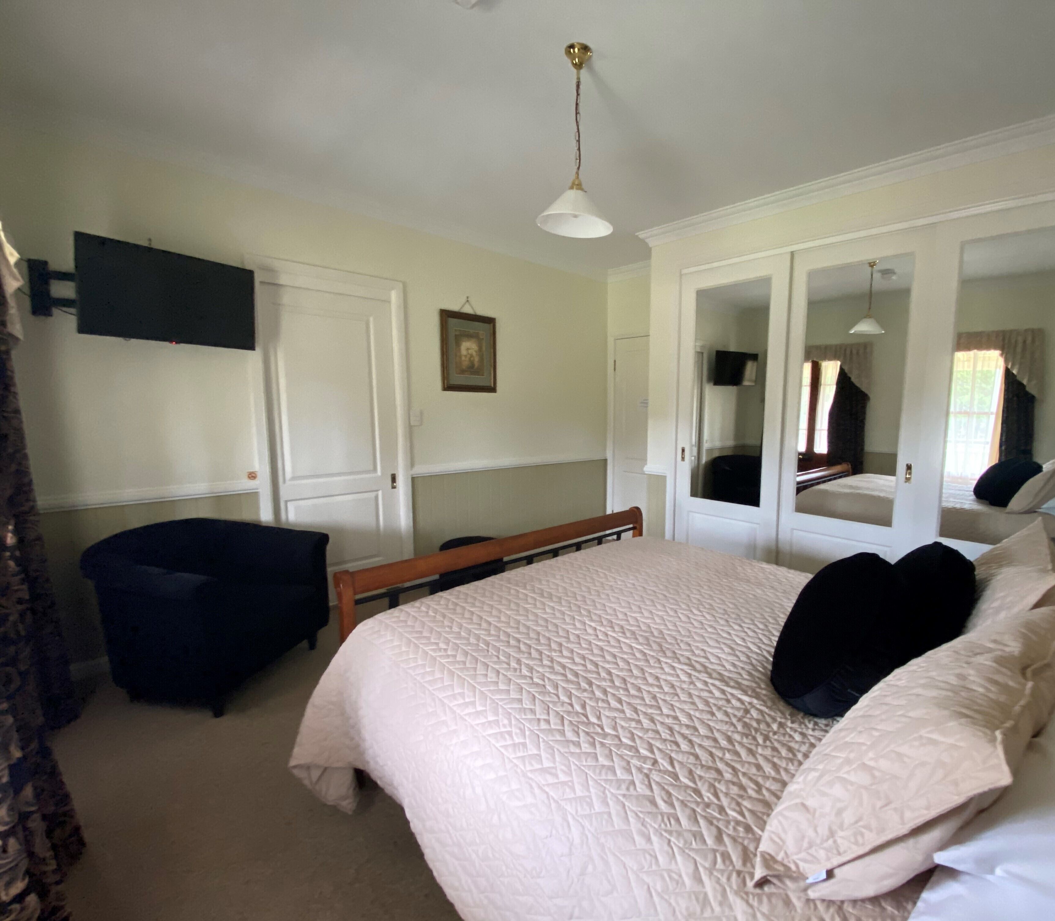 A bedroom with a large bed, a chair, a wardrobe, and a mirror.