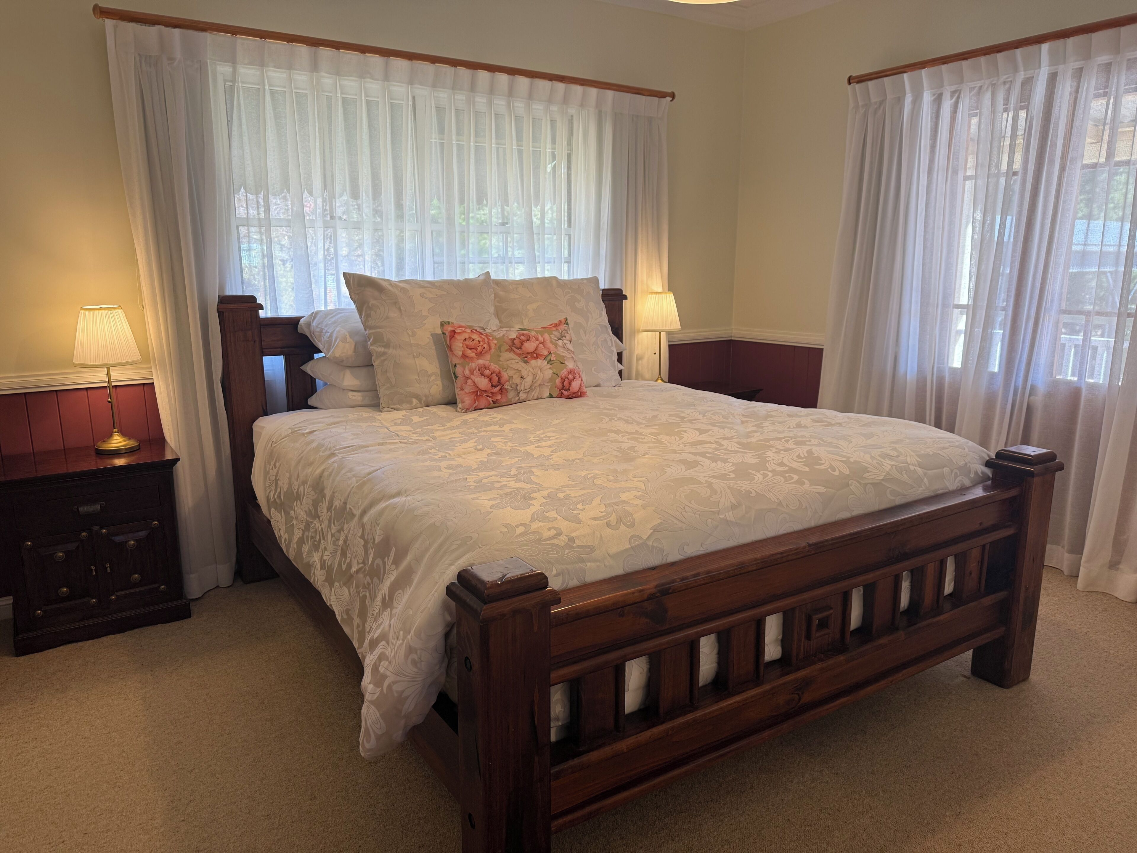 A bedroom with a wooden bed, two bedside tables with lamps, and sheer curtains.