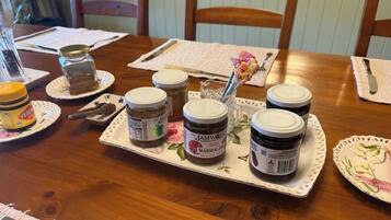 A wooden dining table with a floral tablecloth, a white placemat, and several jars of jam.