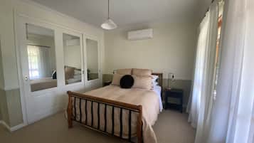 A bedroom with a wooden bed, a bedside table, a lamp, an air conditioning unit, and a mirror.
