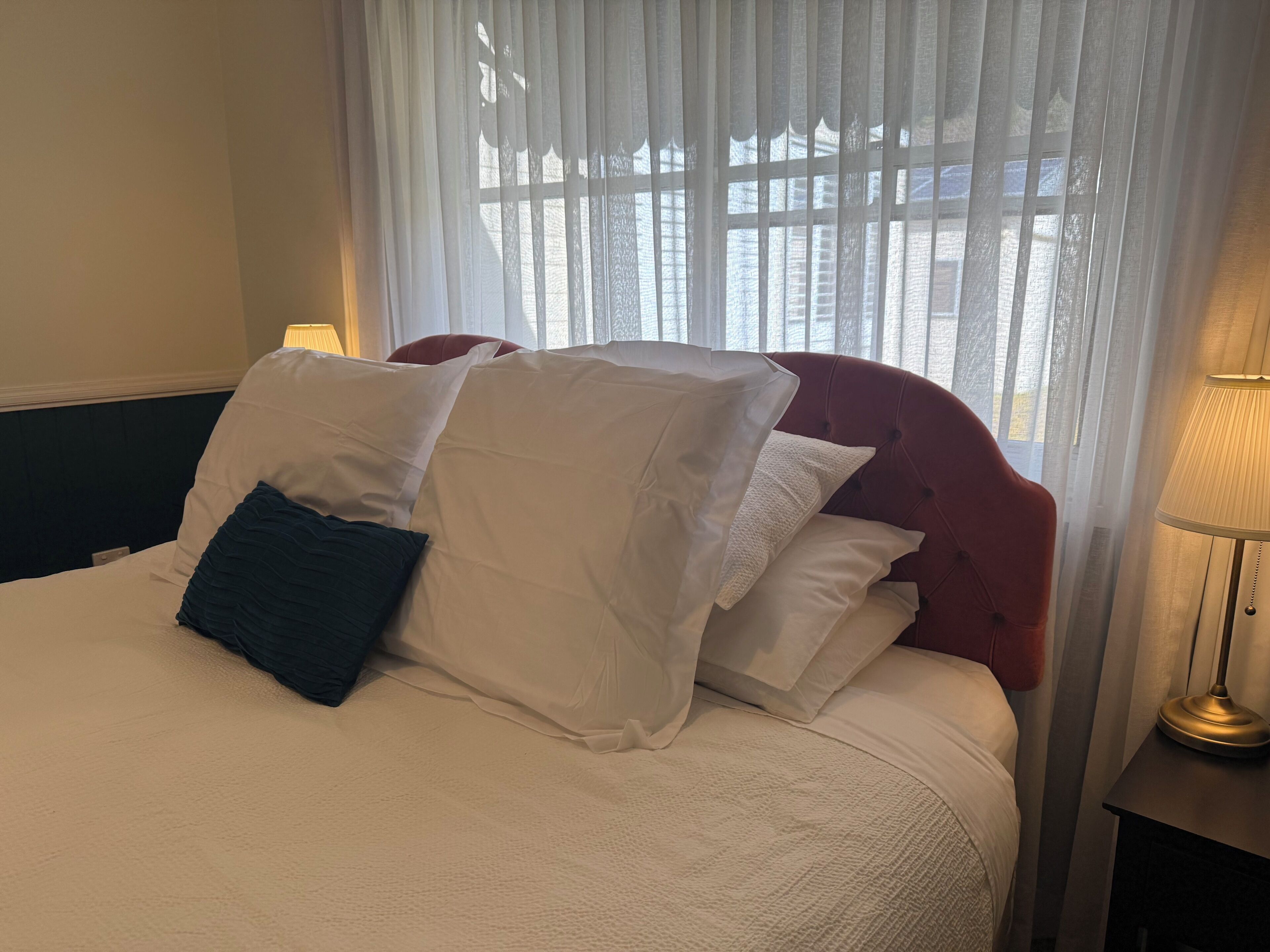 A neatly made bed with white and dark blue pillows, a red headboard, and a lamp on a bedside table.