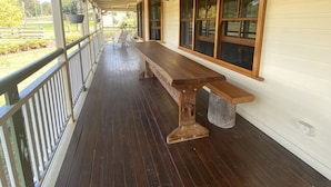 Una terraza cubierta de madera con una banca, ventanas grandes y barandilla.